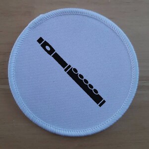 May include: White round fabric patch with a black silhouette of a flute.
