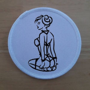 May include: White round patch with a black line drawing of a woman in lingerie. The woman is sitting with her legs crossed and her hands on her thighs.