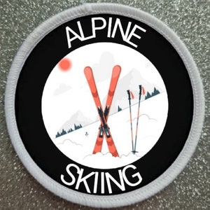 Könnte beinhalten: Ein runder weißer und schwarzer Patch mit dem Text "ALPINE SKIING" in weiß. Der Patch zeigt eine rote und weiße Illustration von Skiern und Skistöcken vor einem weißen Hintergrund mit einer roten Sonne und einem Gebirge.