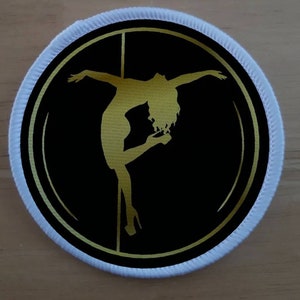 May include: A gold silhouette of a person on a pole dancer against a black background with a gold circle around it. The background is white.