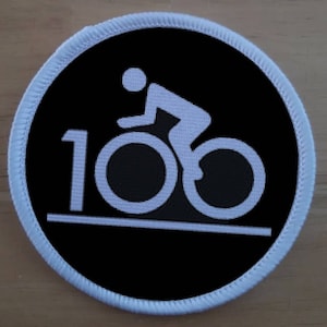 May include: White embroidered patch on a black background with a white silhouette of a person riding a bicycle and the number 100.