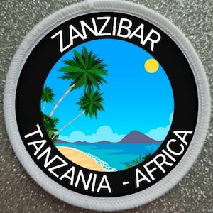 May include: A white round patch with a black circle in the centre. The black circle has white text that reads "ZANZIBAR TANZANIA - AFRICA". Inside the circle is a cartoon image of a beach scene with palm trees, a blue ocean, and a yellow sun.