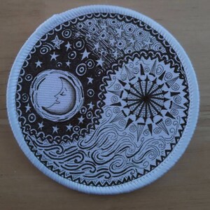 Könnte beinhalten: Runder Aufnäher mit Yin-Yang-Design. Eine Hälfte zeigt einen Mond, Sterne und wellenförmige Linien, die andere ein Sonnenmuster. Das Design ist schwarz-weiß, mit einem weißen Rand.