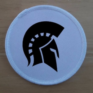 May include: White round fabric patch with a black silhouette of a Spartan helmet.