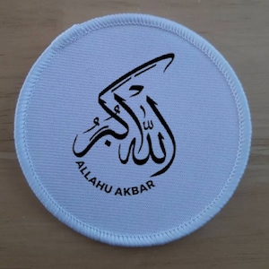 Puede incluir: Parche redondo de tela blanca con caligrafía árabe negra que dice "Allahu Akbar" en inglés.