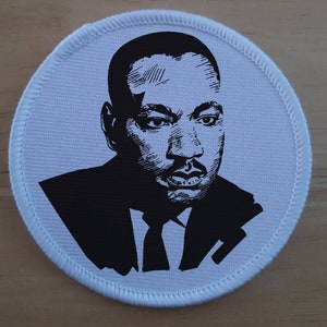 Può includere: Immagine in bianco e nero di Martin Luther King Jr. su una toppa rotonda di tessuto bianco.