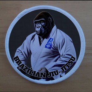 Op de afbeelding: Een witte patch met een zwarte rand en de tekst "Brazilian Jiu-Jitsu" rond de rand. Een gorilla die een witte gi draagt, bevindt zich in het midden van de patch.