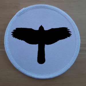 May include: White round fabric patch with a black silhouette of a bird with its wings spread.
