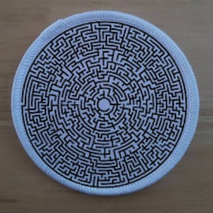 Puede incluir: Parche redondo con un diseño de laberinto en blanco y negro. El laberinto es intrincado y circular, con un borde blanco. El parche se puede usar para decorar ropa o accesorios.