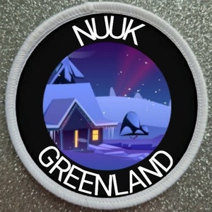 May include: A circular patch with a black border and white stitching. The patch features a winter scene with a house and the text "NUUK GREENLAND" in white. The background shows the aurora borealis.