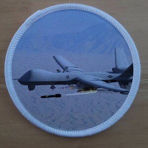 May include: A white military drone with a gray and black missile attached to the underside of the aircraft. The drone is flying over a white, snowy landscape. The drone has the text "422 ATTA" on the side.