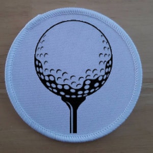 May include: A white round patch with a black and white image of a golf ball on a tee.