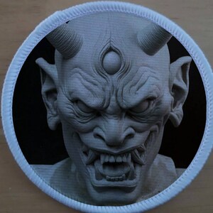 May include: A close-up of a white, detailed, sculpted demon head with horns, a third eye, and a menacing expression. The demon's mouth is open, revealing sharp teeth.