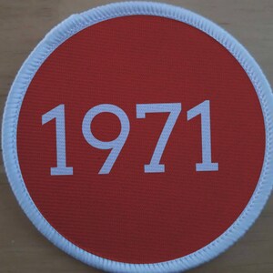 Puede incluir: Un parche circular rojo con un borde blanco y el número 1971 impreso en blanco.