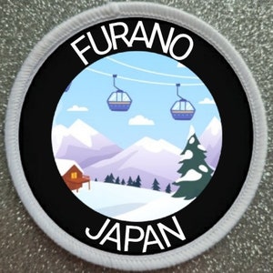 May include: White round patch with black border and text "FURANO JAPAN". Inside the border is a colourful illustration of a snowy mountain scene with ski lifts and a small cabin.