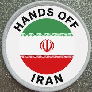 May include: A round patch with the words "HANDS OFF IRAN" in black, arched around the top and bottom. The patch features the Iranian flag's colors: green, white, and red, with the emblem in the center.