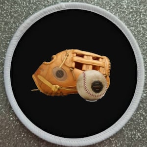 May include: A baseball glove and baseball patch. The baseball glove is tan leather with a webbed pocket. The baseball is white with red stitching and a small, circular label. The patch has a black background and a white border.