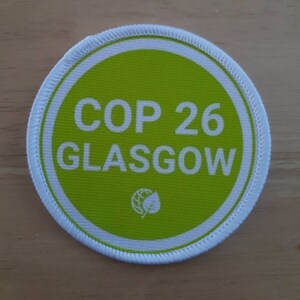 May include: A green and white circular patch with the text "COP 26 GLASGOW" and a small green leaf icon.