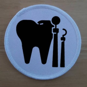 May include: White round fabric patch with a black silhouette of a tooth and dental tools.