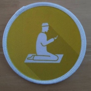 May include: A yellow round patch with a white outline. The patch features a white silhouette of a person kneeling in prayer on a white prayer rug.