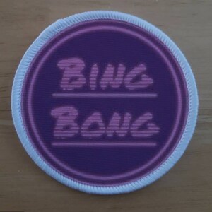 May include: A white oval patch with a purple circle in the center. The circle has the words "Bing Bong" written in pink, with a line separating the two words.