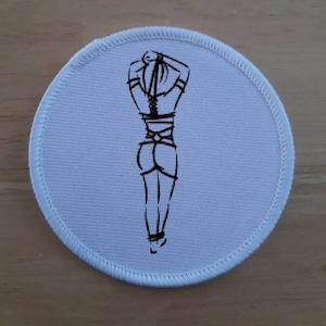 May include: A white round patch with a black line drawing of a person with their hands tied behind their back.