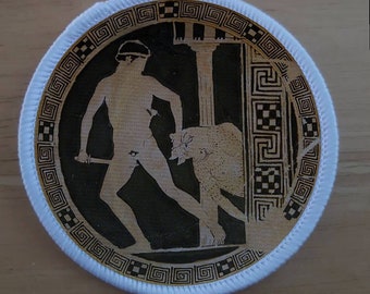 Pode incluir: Remendo redondo com uma ilustração preta e bege de uma cena clássica. Uma figura com uma espada enfrenta uma besta, emoldurada por colunas e uma borda decorativa. O remendo tem uma borda branca.