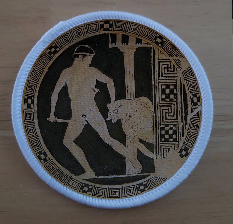 May include: Round patch with a black and beige illustration of a classical scene. A figure with a sword faces a beast, framed by columns and a decorative border. The patch has a white border.