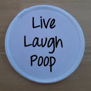 Könnte beinhalten: Runder Stoff-Patch in Weiß mit schwarzem Text, der "Live Laugh Poop" lautet.