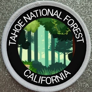 Op de afbeelding: Een witte ronde patch met zwarte tekst en een zwarte cirkel in het midden. De tekst luidt "Tahoe National Forest California". De zwarte cirkel bevat een groene en blauwe illustratie van een bos.