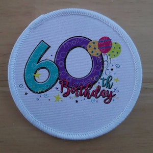 May include: A white round patch with a purple and teal number 60 and the words "60th Birthday" in a colourful font. The number 60 is decorated with yellow stars and the words "60th Birthday" are surrounded by colourful confetti.
