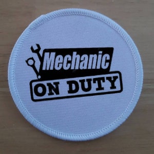 May include: White round fabric patch with black text and a wrench graphic. The text reads "Mechanic On Duty".