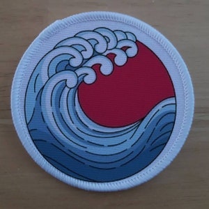 May include: A white embroidered patch featuring a blue and white wave design with a red sun in the background.