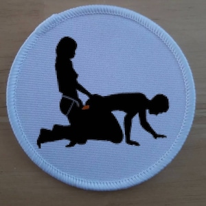 May include: A white round patch with a black silhouette of two figures in a suggestive pose.