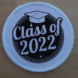 May include: White round fabric patch with a black circle in the centre. The circle has a white graduation cap, the text "Class of 2022" and a white star.