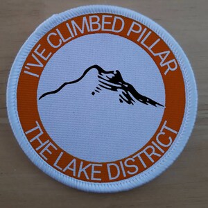 May include: White round patch with an orange border. The text "I've Climbed Pillar The Lake District" is printed in a white circle around a black silhouette of a mountain.