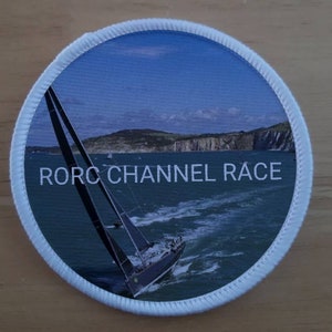 May include: A white round patch with a blue sky and a sailboat in the water. The text "RORC CHANNEL RACE" is printed on the patch.