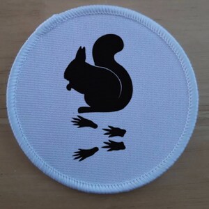 May include: White round fabric patch with a black silhouette of a squirrel and three paw prints.
