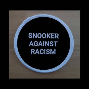 Puede incluir: Un parche redondo blanco y negro con el texto "Snooker Against Racism" en blanco.