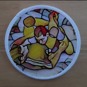 May include: A round, white patch with a colorful image of two figures in a wrestling match. The figures are in a dynamic pose, with one figure on top of the other. The image is stylized and has a stained glass effect.