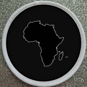 Può includere: Una toppa nera e bianca con un contorno bianco del continente africano. La toppa è circolare e ha un bordo bianco.