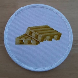 Può includere: Un cerotto rotondo bianco con un design di pallet di legno marrone. Il pallet è impilato su un altro pallet.
