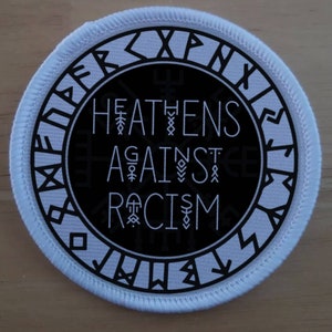 Könnte beinhalten: Ein runder weißer Patch mit schwarzem Text und einem weißen Rand. Der Text lautet "Heathens Against Racism" mit einem stilisierten Runenmuster um den Text herum.