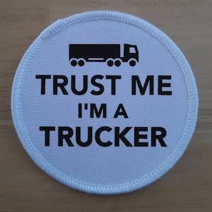 Könnte beinhalten: Runder weißer Aufnäher mit schwarzem Text und einer schwarzen Silhouette eines Lastwagens. Der Text lautet "Vertrau mir, ich bin ein Trucker".
