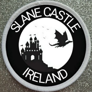 Puede incluir: Parche redondo blanco y negro con el texto "Slane Castle Ireland" en un círculo blanco con un castillo negro y un dragón negro volando por encima.