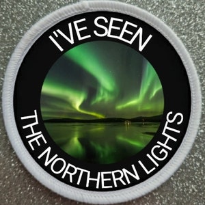 Peut inclure: Un écusson rond blanc avec du texte noir qui dit "I've Seen The Northern Lights" autour d'une photo des aurores boréales reflétées dans un lac.