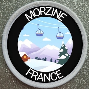 Könnte beinhalten: Ein weißer runder Patch mit schwarzem Text und einem schwarzen Kreis in der Mitte. Der Text lautet "MORZINE FRANCE". Der Kreis enthält eine Cartoon-Illustration einer verschneiten Berglandschaft mit einer Hütte, Bäumen und Skiliften.