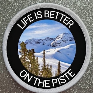 Peut inclure: Patch rond blanc avec une bordure noire et du texte blanc qui dit "Life is better on the piste". Le centre du patch présente une photo d'une chaîne de montagnes enneigées.