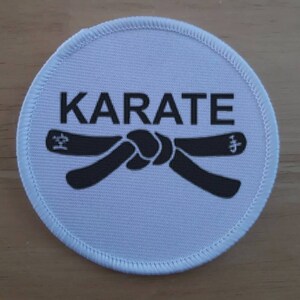 Può includere: Toppa rotonda bianca con testo nero che dice "KARATE" e una cintura nera annodata.