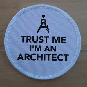 May include: White round fabric patch with black text and a compass symbol. The text reads "Trust me I'm an Architect".